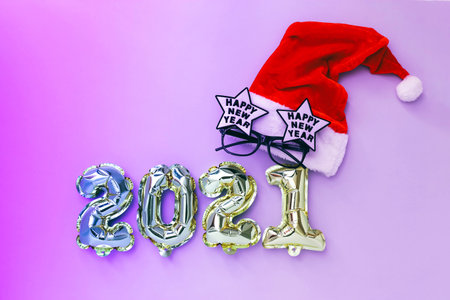 Foil balloons in the form of numbers 2021 and Santa hat with festive glasses, neon effect. New year celebration.の写真素材