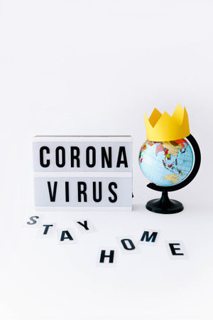 Concept of Covid 19, Corona virus text on display in lightbox and globe with crown on it, light background.の写真素材