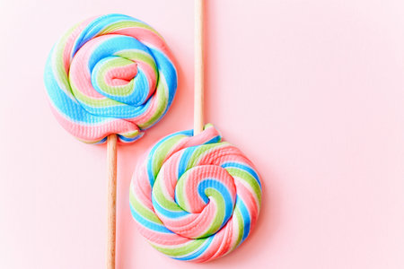Colorful lollipops swirls on sticks. Striped spiral multicolored candy on pink background, top view