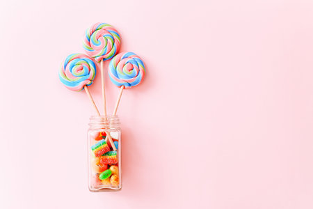 Colorful lollipops swirls on sticks in glass bottle. Striped spiral multicolored candy on pink...