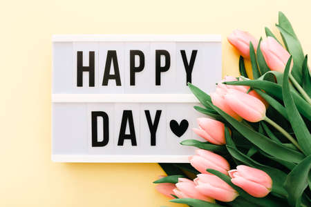 Happy Day words on lightbox with bouquet of pink tulips on light yellow background.の写真素材