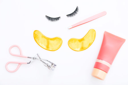 Tools and false eyelashes with golden patches on a white background. The view from the top.