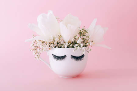 Creative white mug of flowers with long eyelashes on pink background.の写真素材