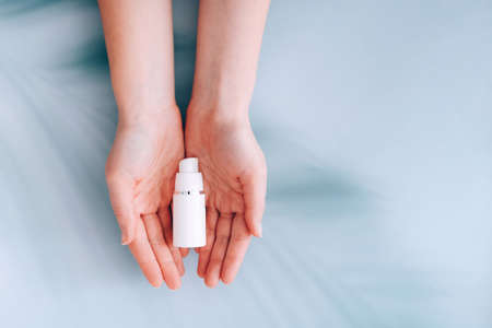 Hands holding skincare cosmetic lotion cream on blue background with palm shadows on itの写真素材