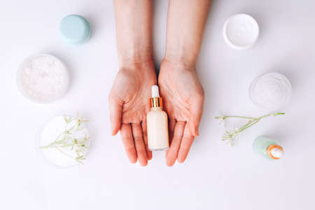 Woman holding bottle of cream over table with cosmetic productsの写真素材