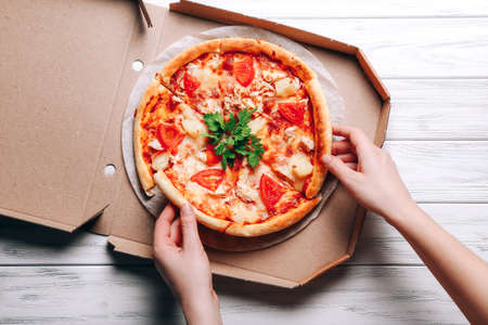 Pizza in delivery box and woman hands taking pizza slices on white wooden backgroundの写真素材
