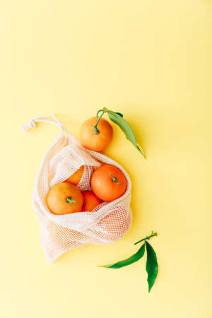 Fresh clementines with leaves in reusable string bag on yellow background, top viewの写真素材
