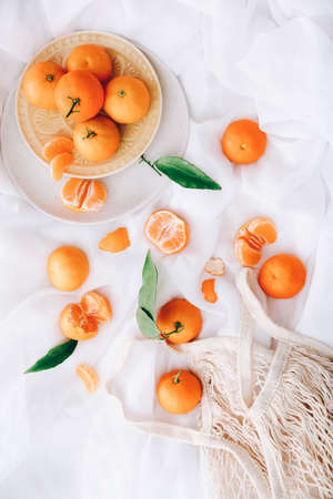 Fresh clementines with leaves and shopping bag on white fabric background, top viewの写真素材