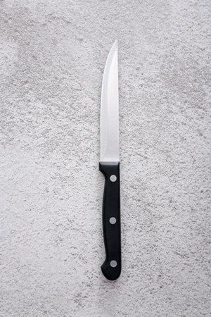 Steel kitchen knife on grey textured background, top view