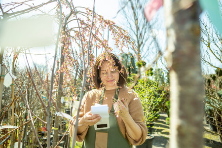A mature woman gardener in a nursery among the trees.