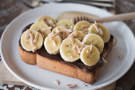 toasted bread topped with chocolate, sliced cavendish banana, sliced almond and honey on a white dishの写真素材