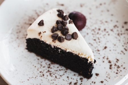 Black beer cake topped with cream cheese and dark chocolate chip served with cherry on a white dish