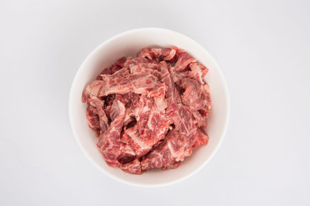 isolated close up flat lay top view shot of sliced raw beef fillet pieces in a white bowl on a white...