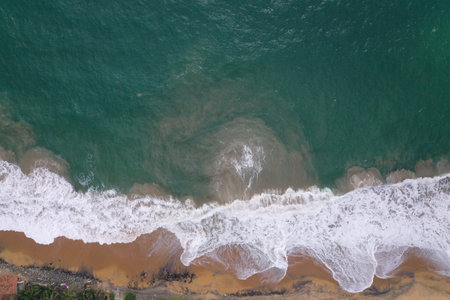 aerial drone bird view shot of the sea shore with turquoise blue water, large white waves and foam,...