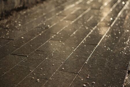 contrasty filled frame background wallpaper photo of dark wet shiny tile with drops of rain and water, reflecting the rays of light of the yellow sunの写真素材