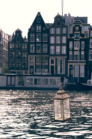 beautiful vertical cityscape shot of a glass candle lantern hanging on Amstel water canal with a house boat, typical narrow dutch houses in the back. Gravelandseveer street, Amsterdam, Netherlandsの写真素材