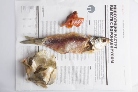 MOSCOW / RUSSIA - 24/05/2020 close up top view shot of a dressed dried salted vobla (Caspian Roach) fish, its separated head, caviar and skin lying on a Russian newspaper backgroundの写真素材