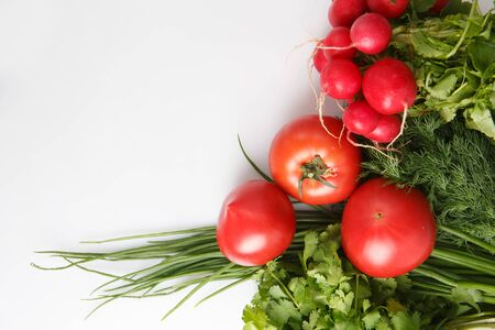 close up top view copy space shot of a vegetable composition consisting of a bunch of radish, dill, parsley, green onions and ripe red tomatoes on a white backgroundの写真素材