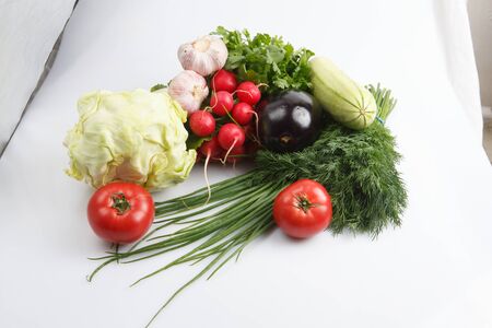close up top view shot of a vegetable salad composition consisting of a bunch of radish, dill, parsley, green onions. aubergine eggplant, zucchini squash, ripe red tomatoes on a white backgroundの写真素材