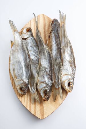 close up top view shot of a bunch of five Russian dried salted vobla (Caspian Roach) fish on a wooden plate on a white backgroundの写真素材