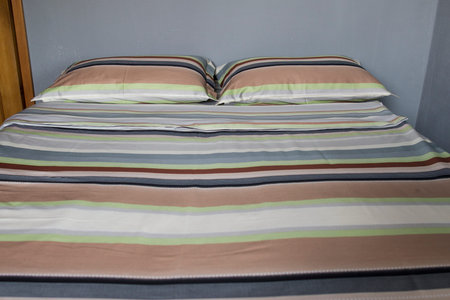 Interior natural light shot of a colorful, striped bed linen with two pillows, a duvet with textile...