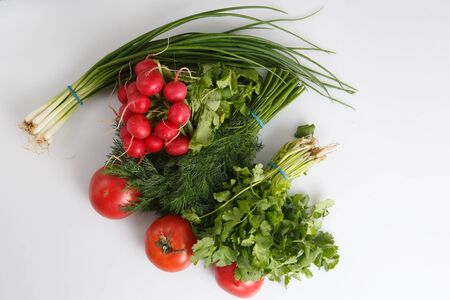 close up top view shot of a vegetable composition consisting of a bunch of radish, dill, parsley, green onions and ripe red tomatoes on a white backgroundの写真素材
