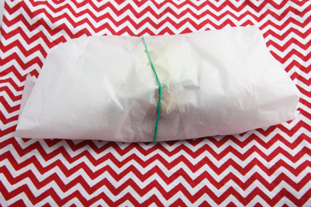 isolated close up shot of a sandwich wrapped in a baking paper wrap package with a green ribbon, on...