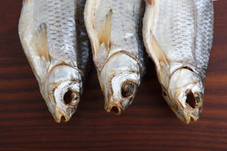 detailed close up top view shot of three Russian dried salted vobla (Caspian Roach) fish on a dark wooden plate backgroundの写真素材