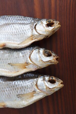 detailed close up top view shot of three Russian dried salted vobla (Caspian Roach) fish on a dark wooden plate backgroundの写真素材