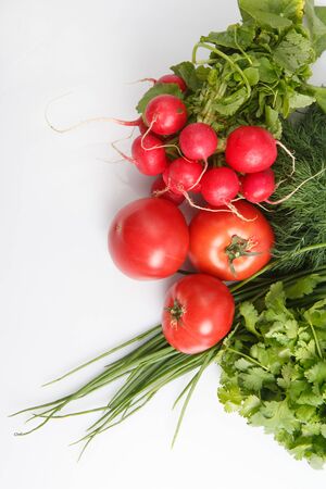 close up top view copy space shot of a vegetable composition consisting of a bunch of radish, dill, parsley, green onions and ripe red tomatoes on a white backgroundの写真素材
