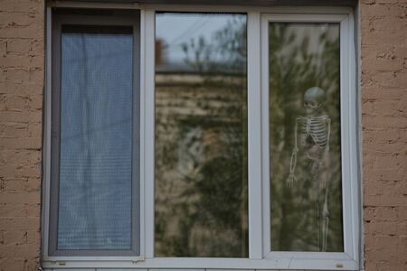 Close up day shot of a human body skeleton figure standing in the corner of a white window frame scaring the people passing byの写真素材
