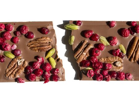 close up shot of a broken chocolate bar with cranberries, hazelnuts and pistachio, broken in half, on a white backgroundの写真素材