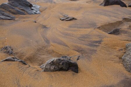 natural filled frame close up wallpaper background early morning photo of sharp brown black rocks on a wet yellow orange sand beach. Sri Lankaの写真素材