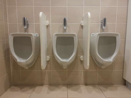 close up of a row of three white ceramic urinals fixed on a beige tile wall separated by privacy wallsの写真素材