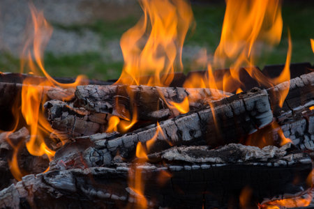 close up shot of log pieces and fire wood, charcoal and ashes burning in a hot oranges flames in an...
