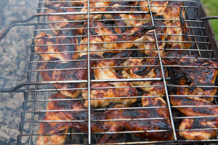 bbq chicken wings in a grill basket grid roasting and cooking on fire and smoke in a barbecue brazierの写真素材
