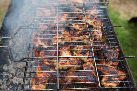 bbq chicken wings in a grill basket grid roasting and cooking on fire and smoke in a barbecue brazierの写真素材