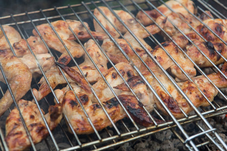 bbq chicken wings in a grill basket grid roasting and cooking on fire and smoke in a barbecue...