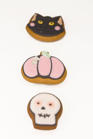 Halloween gingerbread cookies with icing shaped in black cat head, pumpkin and skull in a vertical row of three. Close up shot on a white backgroundの写真素材