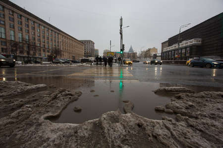 MOSCOW, RUSSIA 01/23/2021 dirty gray black wet sloppy melting snow, slush and ooze, big puddle on asphalt road and people on pedestrian crosswalk. Depressing Winter thaw. Maykovskaya squareのeditorial素材