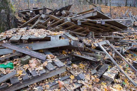 scattered pile of old dirty wooden pallets, wood planks and hardwood timber boards on autumn dry and yellow leaves groundの写真素材