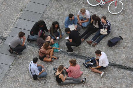 STOCKHOLM, SWEDEN - 09/20/2009 group of young students sitting outside in a street on a cobblestone pedestrian walking road, studying, talking, taking notes, counting money. Aerial summer day shotのeditorial素材