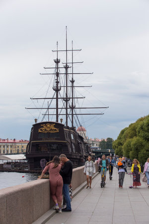 SAINT PETERSBURG, RUSSIA - 08/12/2021 People on embankment. Dutch wooden fluyt merchant sailing ship of the 18th century with three masts (1703 Flying Dutchman restaurant). Gray sky, clouds background.のeditorial素材