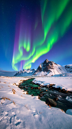 Spectacular green and purple aurora borealis dances in night sky above majestic snowy mountain landscape with flowing river in winterの素材