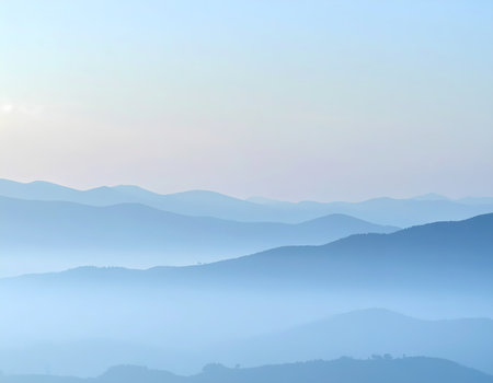 A serene blue mountain range landscape view with layers of haze creating tranquil nature background. soft morning light on distant peak creates peaceful moodの素材