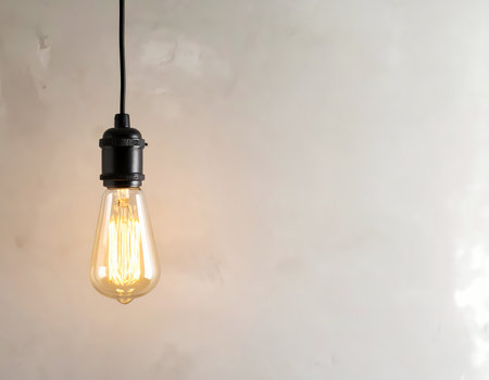 A glowing vintage light bulb hanging against simple background. warm retro lamp offering inspiration and creative idea for interior designの素材