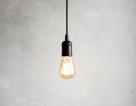 A single hanging light bulb glowing with inspiration, bright idea against gray textured wall. simple minimalist style and creative focusの素材