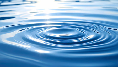 Single drop creates serene ripple circle on calm blue water surface. peaceful liquid wave has bright light reflection, creating tranquil backgroundの素材