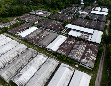 Aerial drone view of an old industrial district with weathered factory building and rusty warehouse roof. desolate and abandoned scene showing structure decay and urban blightの素材