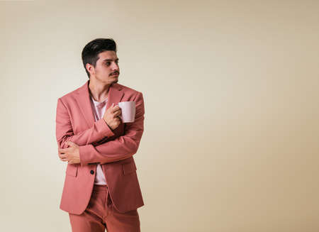 Handsome young man dressed in a pink suit holding a cup facing a blank space on a yellow backgroundの写真素材